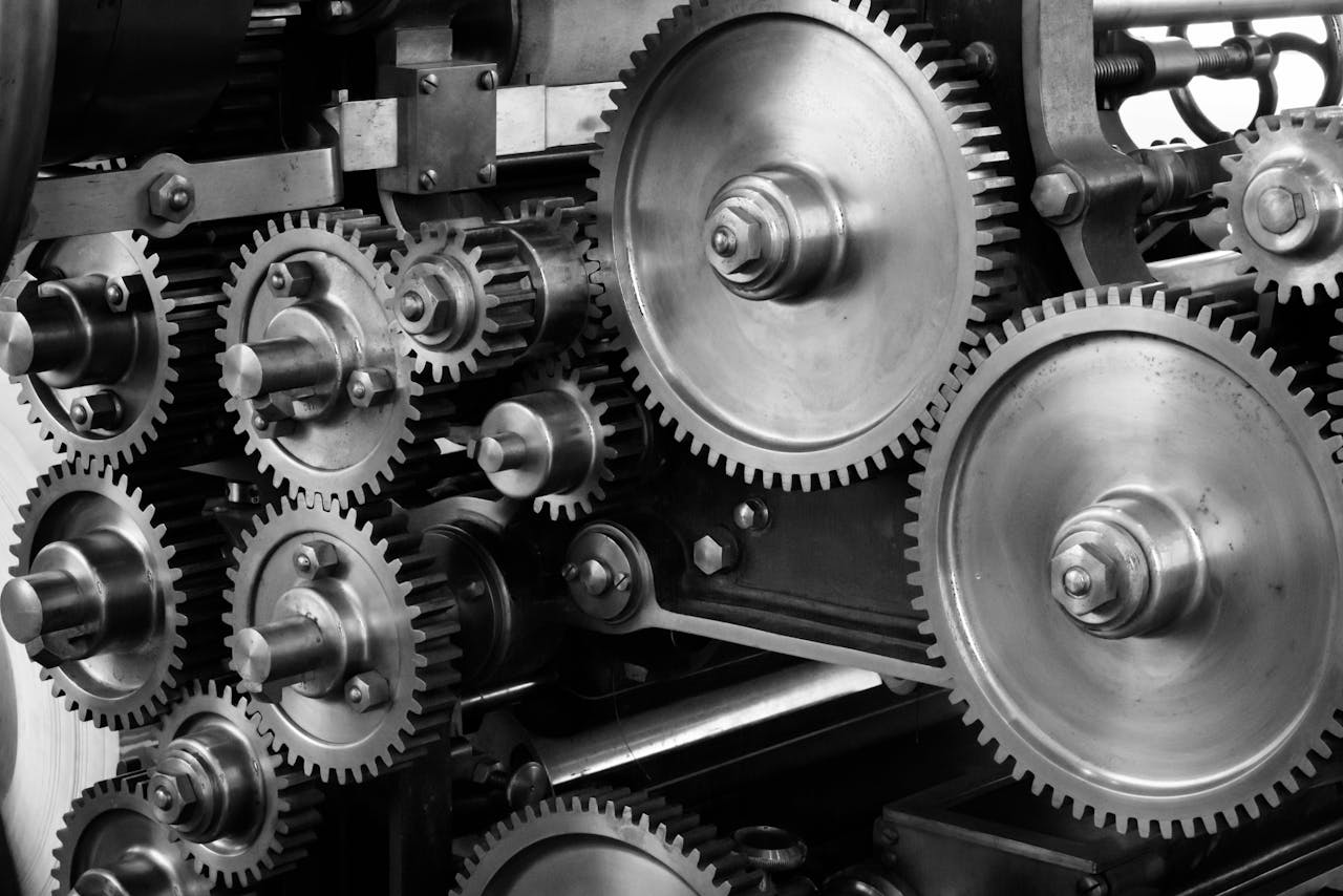 impact-img Close-up view of a complex industrial gear mechanism in black and white.